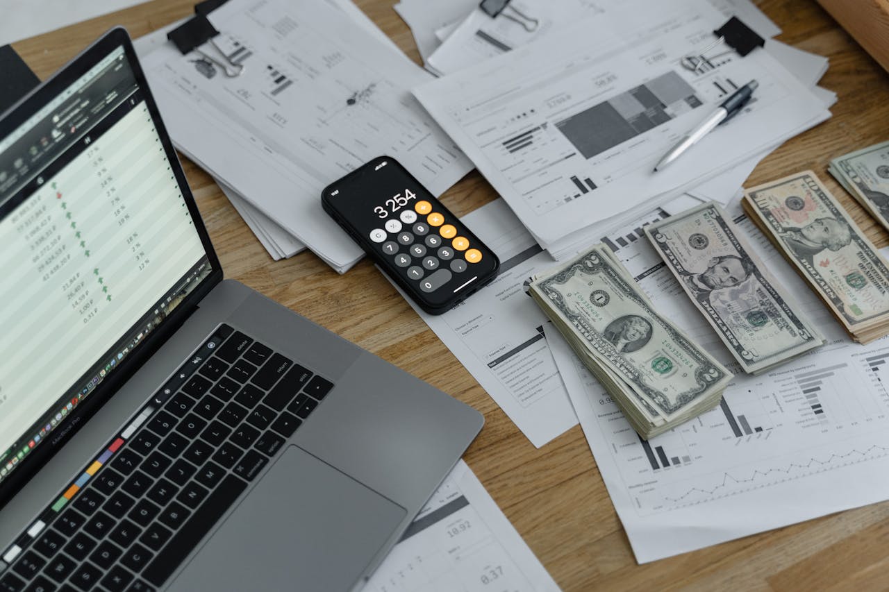 about-02 A desk with financial documents, currency, a laptop, and phone calculator.