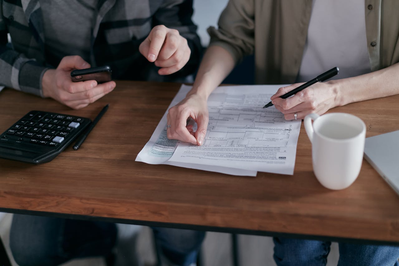 menu-01 Couple managing finances at home with a calculator, smartphone, and documents.