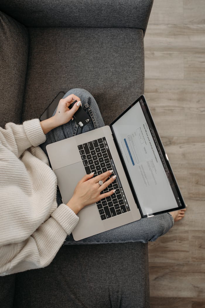 menu-11 Top view of a woman shopping online using a laptop while sitting on a grey sofa.