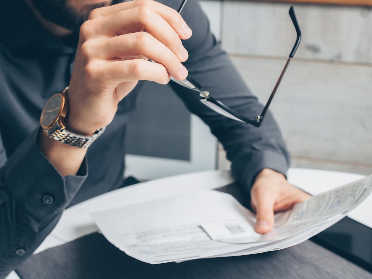 menu-10 Man in formal attire reviewing paperwork, holding glasses. Business setting.